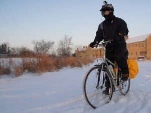 Vintercyklist i mörka kläder trampar genom snö med packväskor
