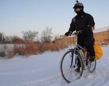 Vintercyklist i mörka kläder trampar genom snö med packväskor