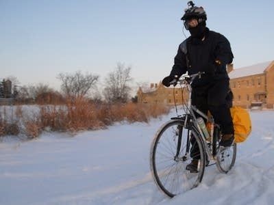 Vintercyklist i mörka kläder trampar genom snö med packväskor