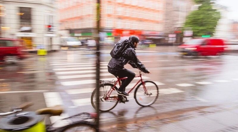 Cyklist i mörka regnkläder pendlar genom en våt stadsmiljö