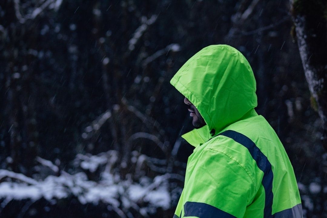 Person i neongrön regnjacka går i mörk, snötäckt skog