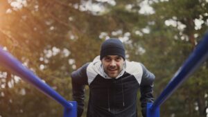 Man i mössa tränar i ett utegym med blå barrar i en skog