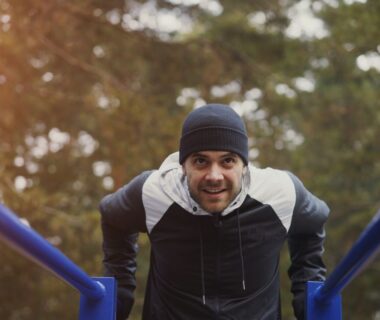 Man i mössa tränar i ett utegym med blå barrar i en skog